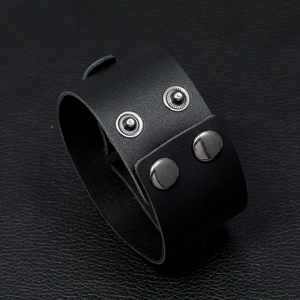 Close-up of black leather wide cuff bracelet with silver snap buttons on textured background
