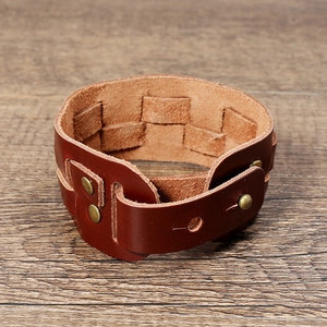 Detail view of woven brown leather bracelet with antique bronze rivets on wood