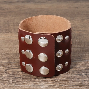 Close-up of wide reddish-brown leather cuff with silver studs on wood background