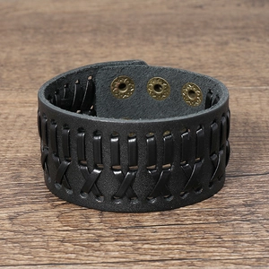 Macro view of woven black leather cuff with bronze adjustable snap buttons on wood