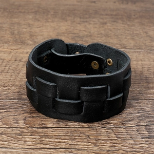 Detail of woven black leather wide bracelet with bronze snap fastener on wood