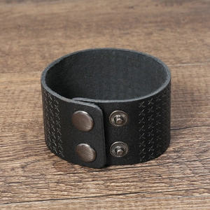 Macro shot of men's wide black leather cuff bracelet with X-shaped embossed patterns