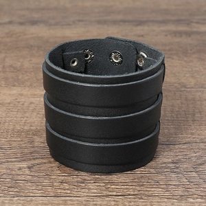 Detail view of the black multi-layer leather cuff bracelet on a wooden background