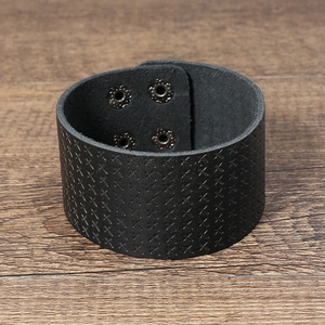 Detail of wide black leather cuff bracelet with cross embossed texture and silver snaps