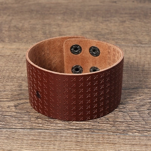 Close-up of wide brown leather bracelet with embossed patterns and silver snap buttons