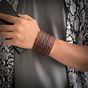 Close-up of wide brown leather bracelet featuring cross-woven cord and stitched edges