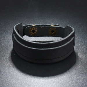 Detail of wide black leather punk bracelet featuring vintage engraved metal snap buttons