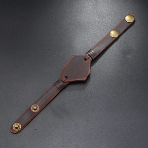 Dettaglio del bracciale in pelle marrone vintage con scudo e bottoni automatici in bronzo