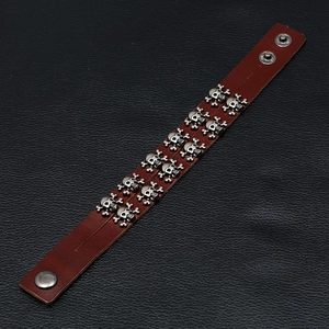 Detail of double-row silver skull studs on dark brown leather punk bracelet with snaps