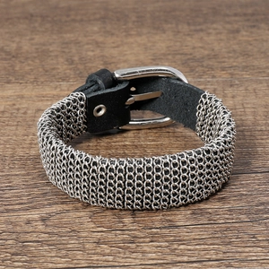 Macro shot of silver woven metal mesh chain with a black leather buckle on wooden desk