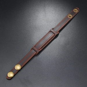 Macro detail of vintage brown leather bracelet with brass snap buttons on grey sand texture