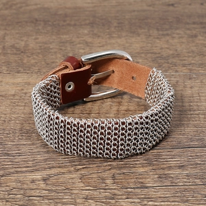 Detail of metal woven bracelet with brown leather strap and pin buckle on wood background