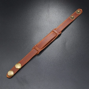 Detail of vintage brown leather bracelet with dual brass snap buttons on black background
