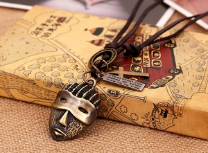 Macro detail of vintage bronze mask pendant with cross on brown leather necklace