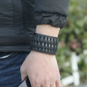 Gros plan d'un bracelet large en cuir tressé noir porté avec une tenue décontractée
