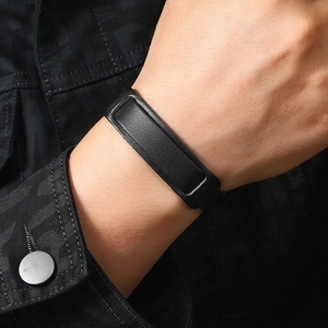 Close-up of a wide minimalist black leather bracelet worn on a wrist with denim background