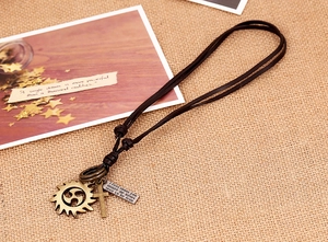 Detail of vintage leather necklace with bronze sun gear and cross charms on linen fabric