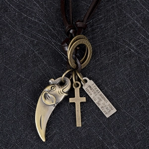 Gros plan de pendentifs éléphant et croix vintage sur un cordon en cuir tressé brun