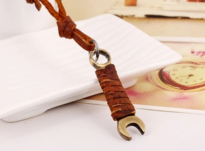 Macro shot of industrial retro wrench pendant with brown leather cord detail on a white tray