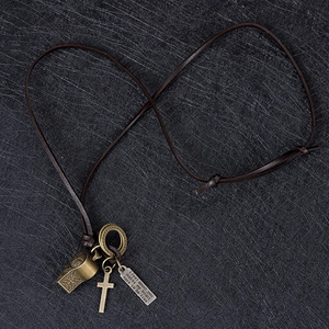 Dettaglio di una collana vintage in pelle con ciondoli a fischietto e croce in bronzo antico