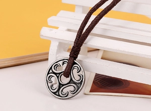 Macro detail of antique silver circular pendant with hollow patterns on brown braided cord