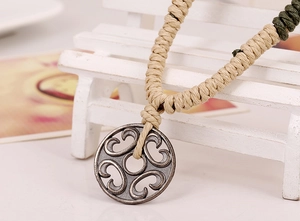 Close-up of vintage hollow alloy pendant with handmade woven rope on a wooden bench