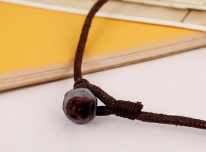 Macro detail of dark brown waxed cord necklace with industrial metal nut and hand-knit knot