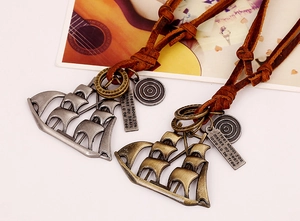 Close-up of vintage sailboat pendants and brown leather cord on artistic background