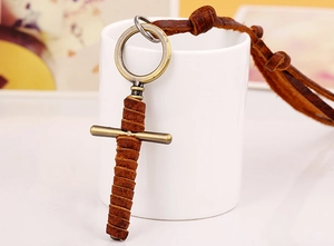 Close-up of vintage bronze cross pendant with brown leather cord on a ceramic cup
