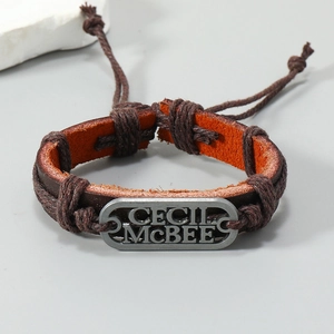 Détail du bracelet en cuir tressé avec plaque métallique gravée sur surface en marbre