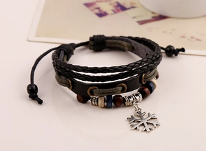 Dettaglio di un bracciale in pelle intrecciata con perline di legno e ciondolo a fiocco di neve