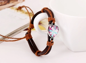 Dettaglio del bracciale in pelle intrecciata con pendente a cuore su tazza bianca
