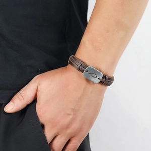 Detail of a brown braided leather bracelet featuring a silver metal plate with a fish symbol