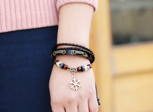 Dettaglio di un bracciale multistrato in pelle intrecciata con perline in legno e fiocco neve