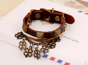 Close-up of leather bracelet featuring bronze clover charms and rivets on a gift box