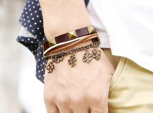 Close-up of multilayer leather bracelet with bronze four-leaf clover charms on a wrist