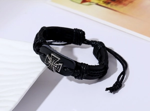 Macro detail of braided black leather bracelet featuring a vintage silver metal cross icon