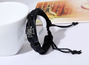 Detail of black woven leather bracelet featuring a silver metal cross on a white mug