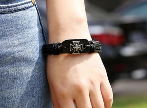 Outdoor close-up of a vintage black braided leather bracelet featuring an iron cross charm