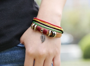 Detail of multi-layer woven bracelet with silver leaf pendant and leather band on wrist