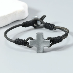 Détail d'un bracelet en corde de cuir noir tressé avec un pendentif croix en métal mat