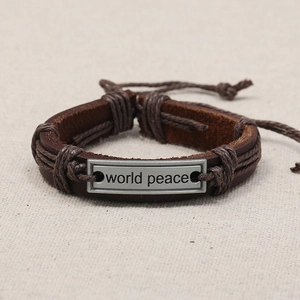 Vintage leather braided bracelet with World Peace engraved metal plate on beige canvas