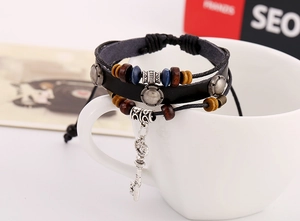 Close-up of multilayer black leather bracelet featuring wooden beads and vintage key charm
