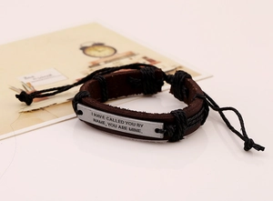 Close-up of vintage brown leather bracelet with engraved metal quote plate and cord