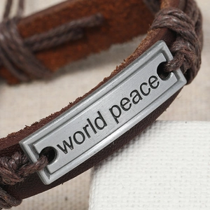 Macro shot of World Peace engraved metal plate on vintage braided leather bracelet