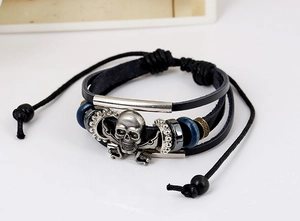 Macro detail of multi-layer leather bracelet with silver skull and crossbones charm