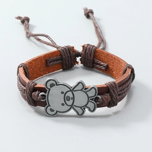 Detail eines braunen Vintage-Lederarmbands mit geflochtenem Seil und silbernem Bärenanhänger