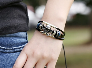 Detailed close-up of multilayer leather bracelet with silver skull and sword charms