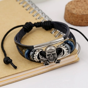 Multilayer braided leather bracelet with skull motif and metal beads on notebook