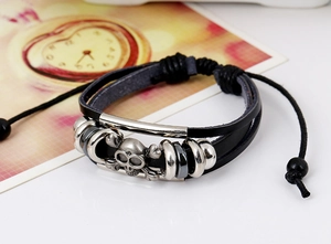 Dettaglio di bracciale punk in pelle con teschio in metallo e cordini intrecciati multistrato